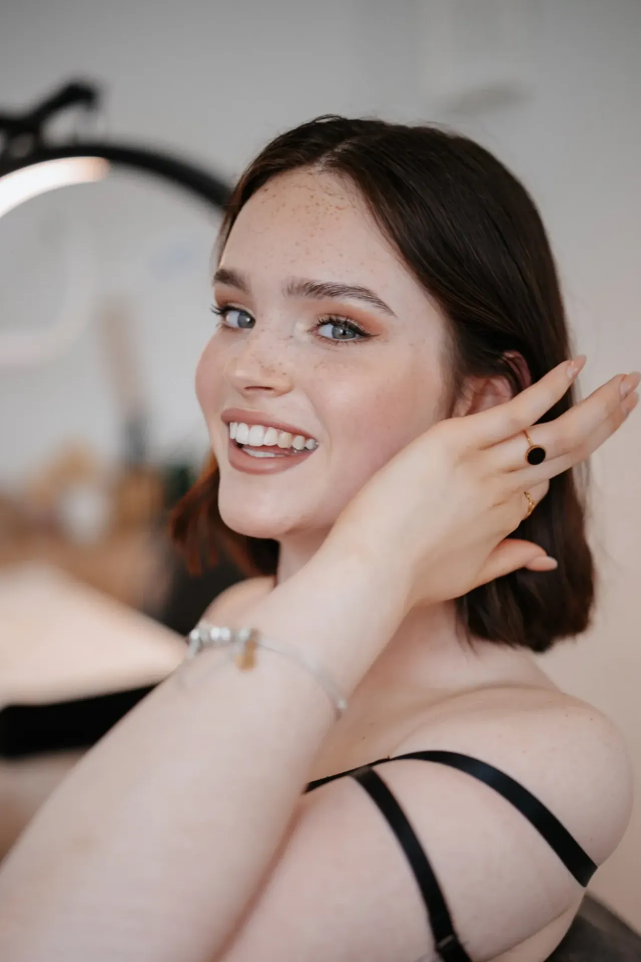 Lachende Kundin mit fertigem Make-up, im Hintergrund ein Ringlicht