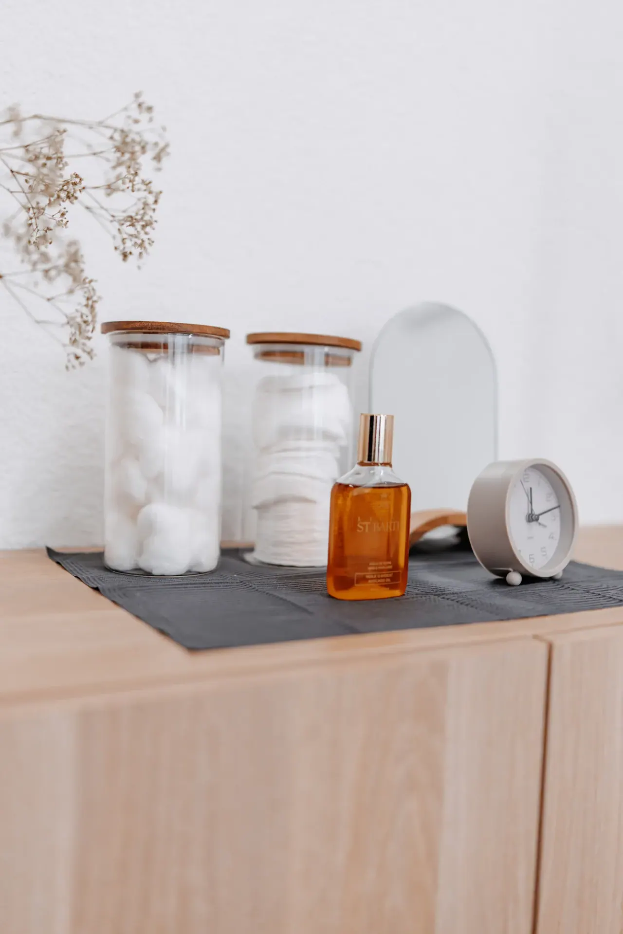 Glasbehälter mit Wattepads, eine braune Glasflasche und eine kleine Uhr auf dem Sideboard im Studio